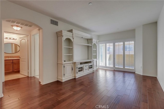 unfurnished living room featuring arched walkways, dark wood-style flooring, visible vents, and baseboards