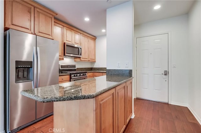 kitchen featuring dark stone counters, appliances with stainless steel finishes, wood finished floors, light brown cabinetry, and recessed lighting