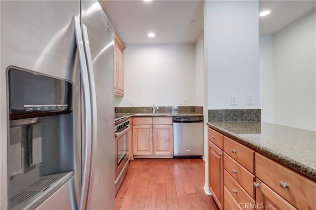 kitchen with dark stone counters, light wood-style flooring, appliances with stainless steel finishes, a sink, and recessed lighting