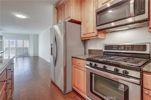 kitchen featuring light brown cabinets, light stone counters, stainless steel appliances, and wood finished floors