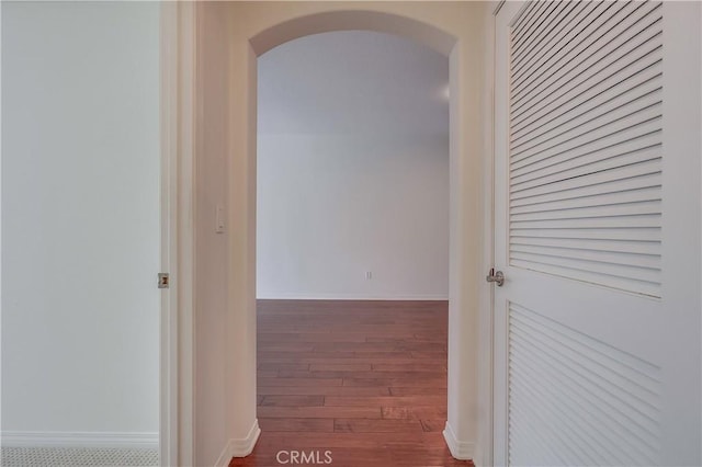 hallway with baseboards, arched walkways, and wood finished floors