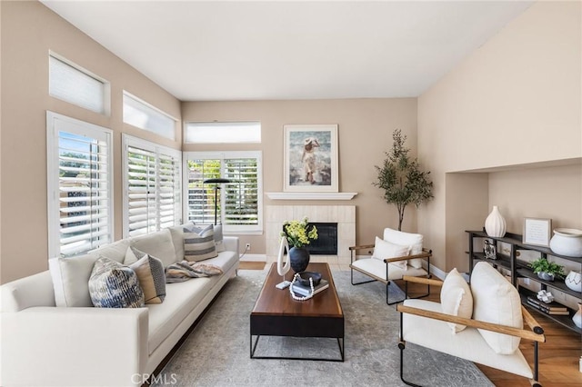 living area featuring a tiled fireplace, baseboards, and wood finished floors