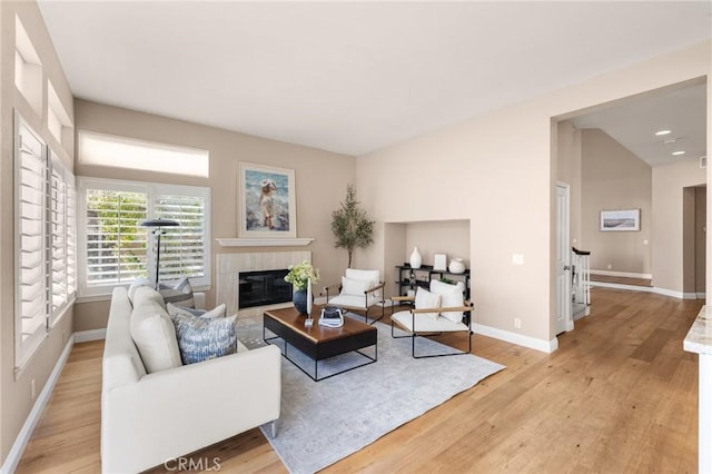 living area featuring lofted ceiling, a fireplace, baseboards, and light wood finished floors