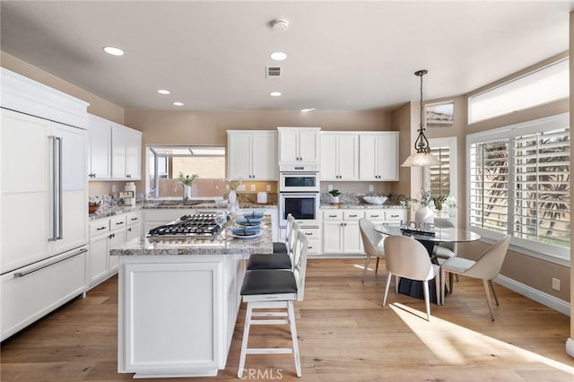 kitchen featuring white double oven, a center island, stainless steel gas cooktop, paneled built in fridge, and white cabinetry