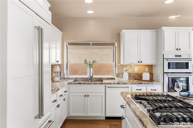 kitchen with light stone countertops, stainless steel gas cooktop, a sink, white cabinets, and white double oven