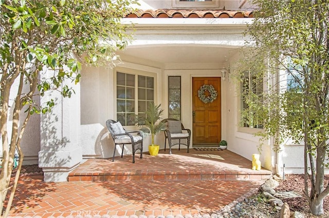 entrance to property with a tiled roof, a porch, and stucco siding