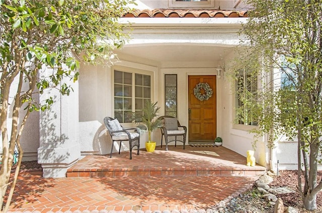doorway to property featuring stucco siding, covered porch, and a tiled roof