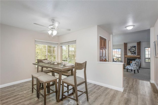 dining room with a textured ceiling, a brick fireplace, wood finished floors, and baseboards