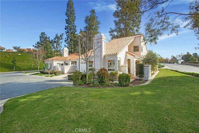 mediterranean / spanish house with driveway, a tile roof, a chimney, a front lawn, and stucco siding