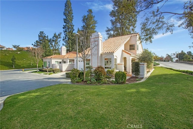 view of front of house with a chimney, stucco siding, a tile roof, and a front yard
