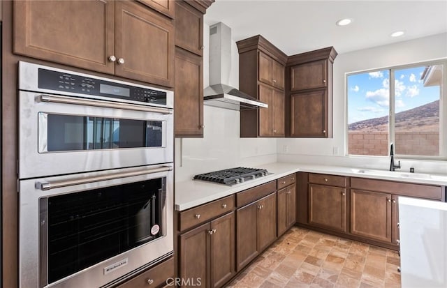 kitchen with recessed lighting, light countertops, appliances with stainless steel finishes, a sink, and wall chimney exhaust hood