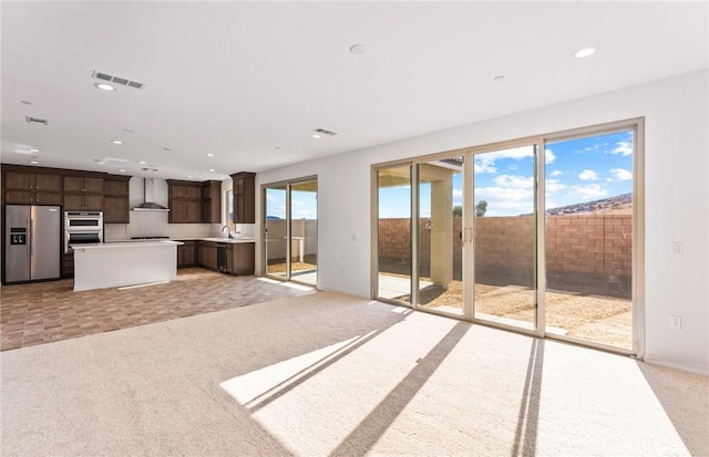 unfurnished living room with light carpet, a sink, visible vents, and recessed lighting