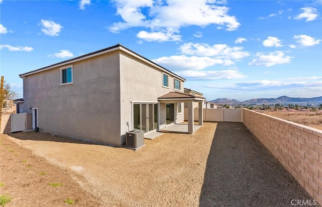 view of side of home with a patio, central AC unit, a fenced backyard, a mountain view, and stucco siding