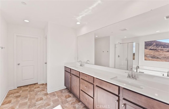 bathroom featuring double vanity, a stall shower, a sink, and baseboards