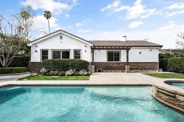 rear view of property featuring an in ground hot tub, a chimney, stucco siding, and an outdoor pool