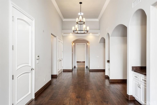 corridor with baseboards, arched walkways, dark wood-style flooring, an inviting chandelier, and crown molding