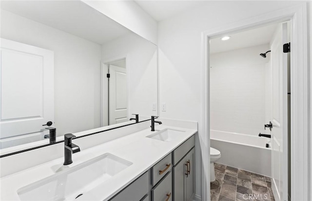 full bathroom featuring toilet, double vanity, stone finish floor, and a sink