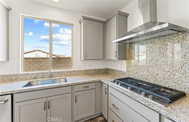 kitchen with stainless steel appliances, backsplash, gray cabinetry, a sink, and wall chimney exhaust hood