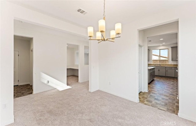 unfurnished dining area featuring carpet floors, visible vents, baseboards, and an inviting chandelier