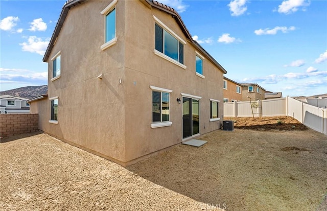 rear view of property featuring central AC unit, a fenced backyard, and stucco siding