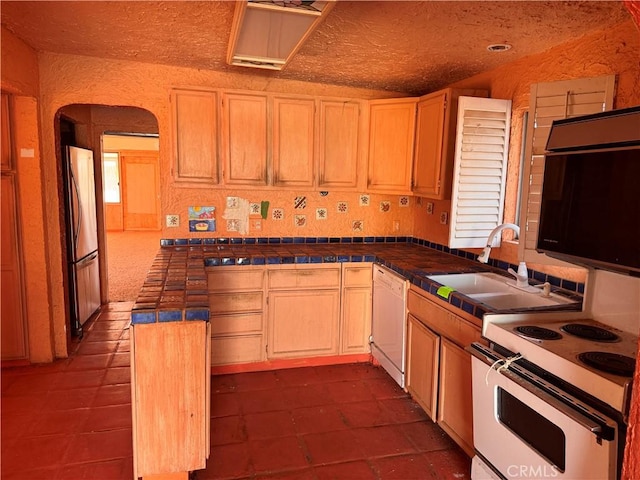 kitchen featuring a sink, white appliances, arched walkways, a peninsula, and tile counters