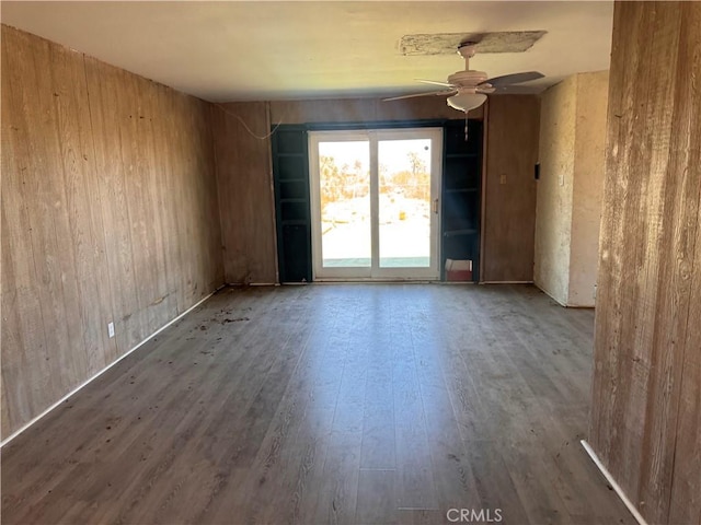 spare room with a ceiling fan, wood finished floors, and wood walls