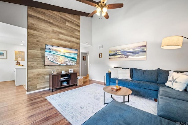 living area with visible vents, a high ceiling, ceiling fan, wood walls, and wood finished floors