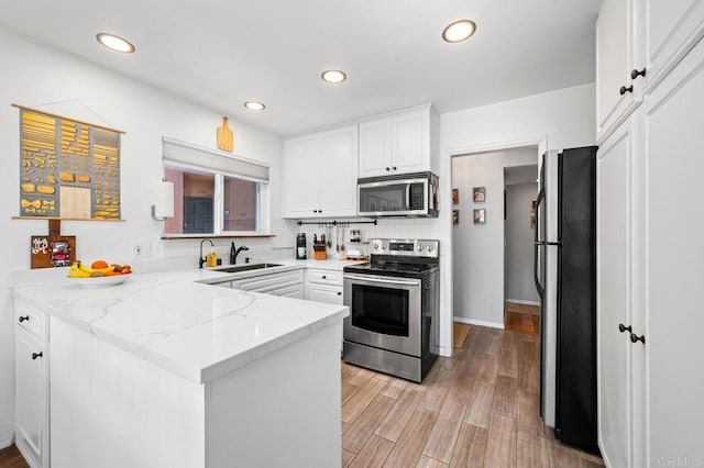 kitchen featuring tasteful backsplash, appliances with stainless steel finishes, a peninsula, white cabinetry, and a sink