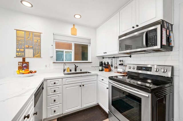 kitchen featuring appliances with stainless steel finishes, white cabinetry, a sink, and tasteful backsplash