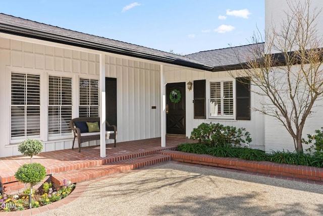 doorway to property with covered porch, board and batten siding, and roof with shingles