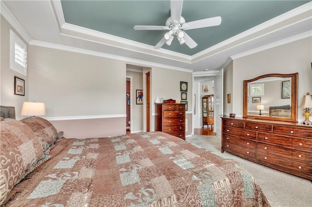 carpeted bedroom with ornamental molding, a tray ceiling, and a ceiling fan