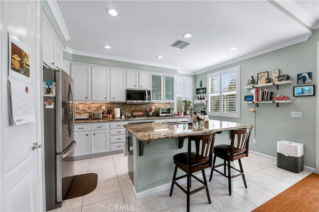 kitchen featuring stainless steel appliances, ornamental molding, white cabinetry, a sink, and a kitchen breakfast bar