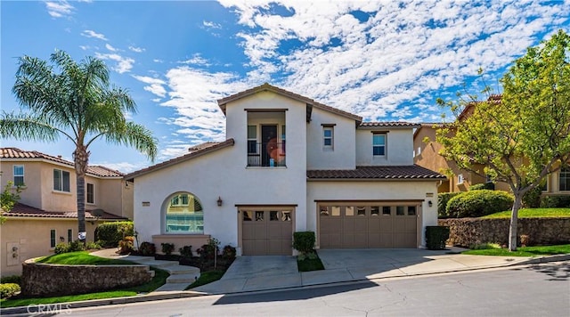 mediterranean / spanish-style home with driveway, a tiled roof, an attached garage, and stucco siding