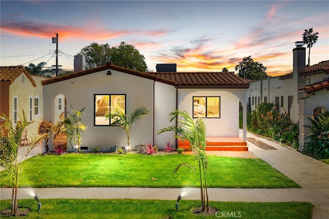 mediterranean / spanish home featuring a tile roof, a yard, and stucco siding