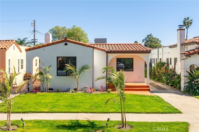 mediterranean / spanish home with a tiled roof, a front lawn, and stucco siding