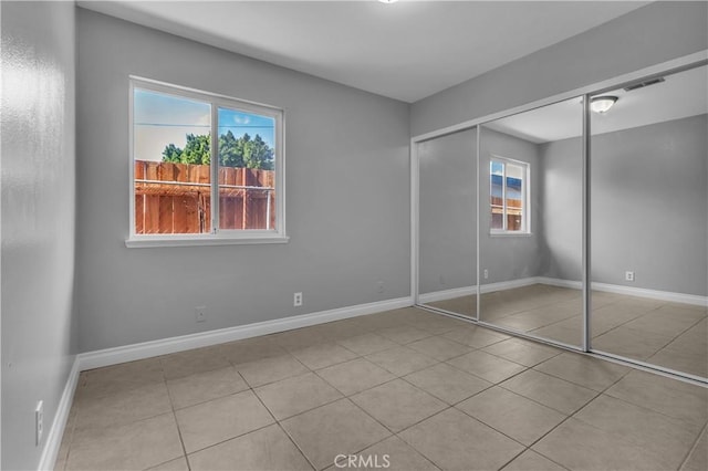 unfurnished bedroom with tile patterned flooring, a closet, and baseboards