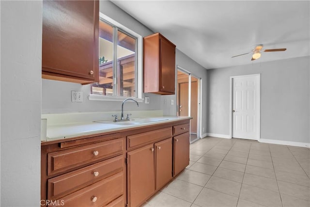 kitchen featuring light countertops, light tile patterned flooring, ceiling fan, a sink, and baseboards