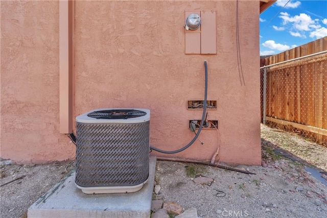 exterior details featuring stucco siding, cooling unit, and fence