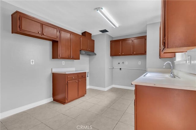 kitchen with under cabinet range hood, brown cabinetry, a sink, and light countertops