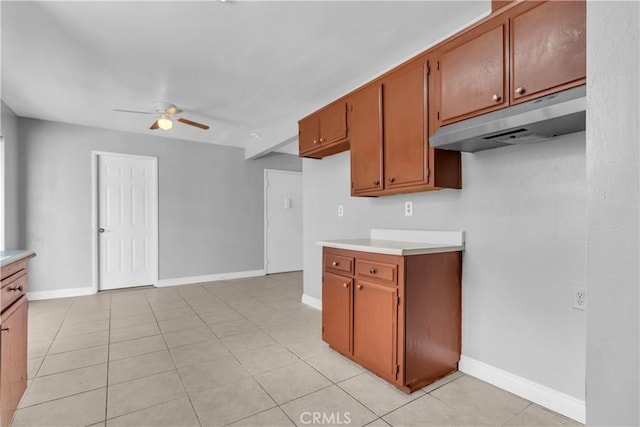 kitchen with light countertops, a ceiling fan, brown cabinetry, under cabinet range hood, and baseboards