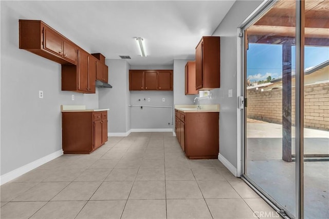 kitchen with light tile patterned floors, visible vents, baseboards, light countertops, and brown cabinetry