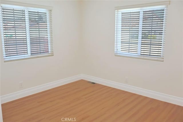 spare room featuring wood finished floors, visible vents, and baseboards