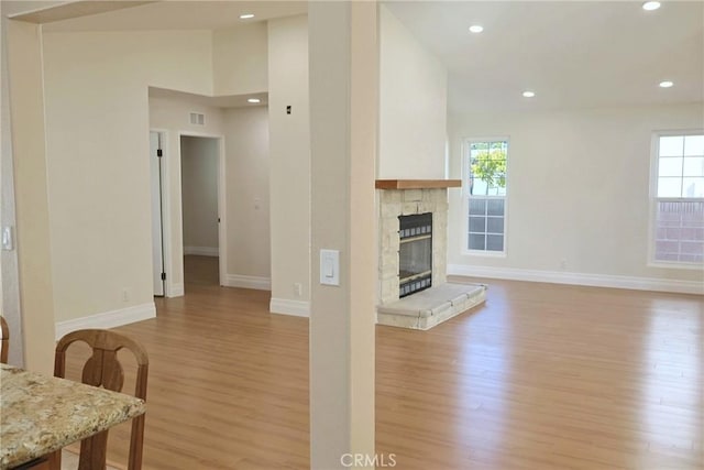 living area with visible vents, baseboards, a stone fireplace, light wood-type flooring, and recessed lighting