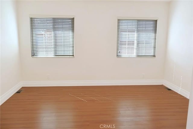 unfurnished room with visible vents, plenty of natural light, baseboards, and wood finished floors