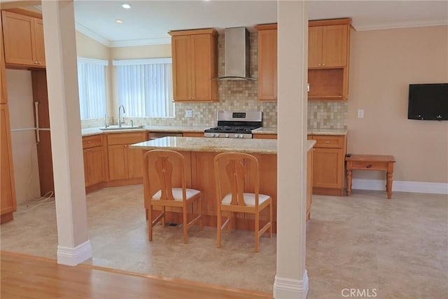 kitchen with ornamental molding, stainless steel range with gas stovetop, a kitchen island, a sink, and wall chimney exhaust hood