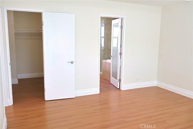 unfurnished bedroom featuring a walk in closet, a closet, light wood-style flooring, and baseboards