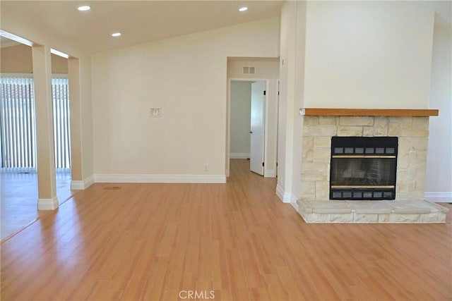 unfurnished living room featuring lofted ceiling, a stone fireplace, wood finished floors, and baseboards