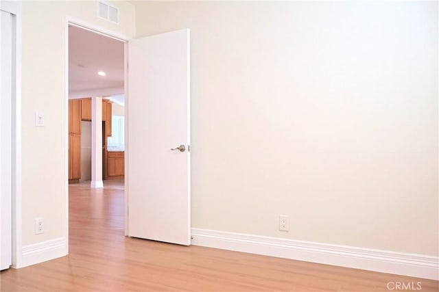 empty room with light wood finished floors, visible vents, and baseboards