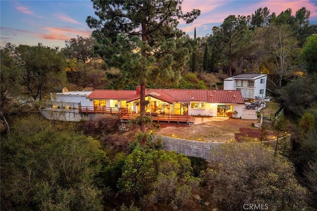 back of property at dusk with a chimney, a deck, and a tiled roof