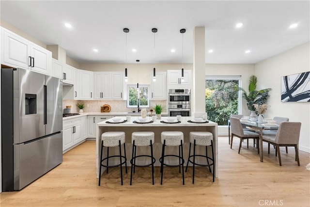 kitchen featuring white cabinets, appliances with stainless steel finishes, a breakfast bar area, a center island, and light wood-type flooring